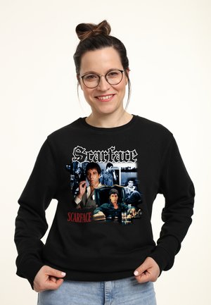 Schwarzer Hoodie mit "Scarface"-Grafiken, verschiedenen Bildern von Charakteren und Titeltext in Weiß und Rot, der prominent auf der Vorderseite dargestellt ist.