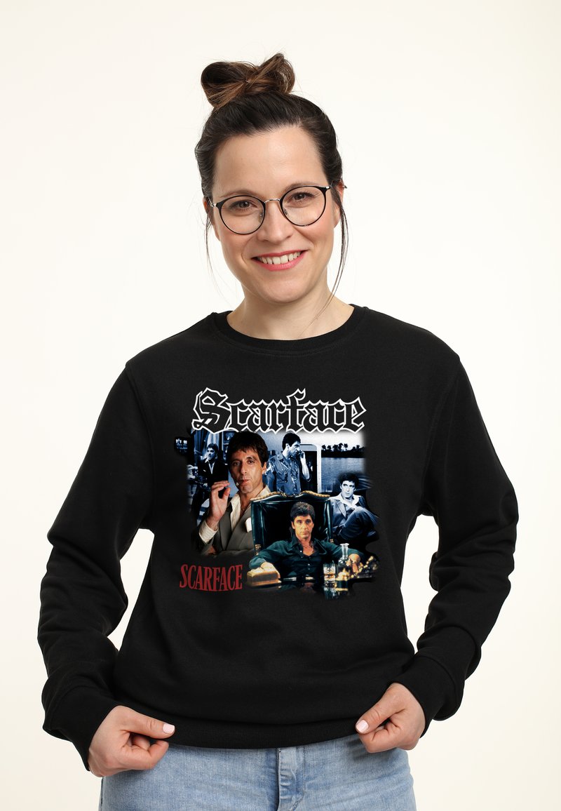 Felpa nera con grafiche di "Scarface", assortimento di immagini dei personaggi e testo del titolo in bianco e rosso, mostrato in modo prominente sul davanti.