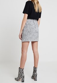 Černý top s krátkým rukávem v kombinaci s texturovanou šedou mini sukní. Modelka má na sobě kotníkové boty s hadím vzorem a blokovým podpatkem.
