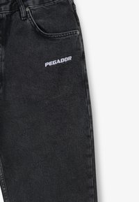 Černé džíny z denimu s texturovanou látkou, vybavené přední kapsou a na levé nohavici vyšitým nápisem "PEGADOR" v bílé barvě.