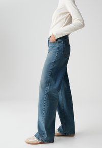 Light blue high-waisted wide-leg jeans with a faded finish, featuring a classic five-pocket design and minimal distressing, paired with beige sneakers.