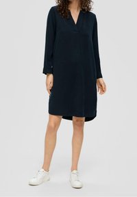 Granatowa sukienka z dekoltem w serek, z długimi rękawami i luźnym krojem, z asymetrycznym dołem. Poł�ączona z białymi sneakersami dla swobodnego wyglądu.