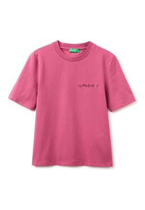 Camiseta rosa de manga corta con cuello redondo, con la palabra "amour" bordada en cursiva pequeña en el pecho izquierdo y una etiqueta verde dentro del cuello.