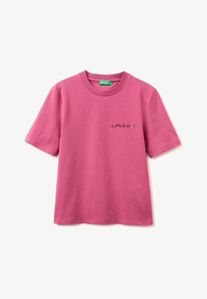 T-shirt rose à manches courtes col rond avec « amour » brodé en petite écriture cursive sur la poitrine gauche et une étiquette verte à l’intérieur du col.