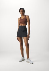 Brun sports bh, sort nederdel og hvide sneakers. Nederdelen har en glat tekstur, mens bh'en har et tætsiddende design med tynde stropper.