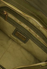 Interno di borsa in pelle verde oliva con molteplici tasche con zipper. Accessori in tonalità oro e un'etichetta con la scritta "CATERINA LUCCHI MADE IN ITALY."