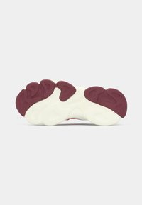 Sneaker outsole featuring a white midsole with a textured surface and maroon rubber pods in a wavy design for traction and grip.