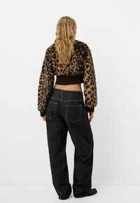 Giacca cropped in pelliccia sintetica con motivo leopardato, nei colori marrone e beige. Abbinata a jeans in denim scuro a vestibilità ampia.