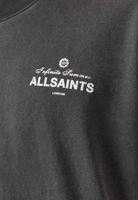 Mørkegrått stoff med hvit trykt tekst "Infinite Summer ALLSAINTS LONDON" og et lite blomsteremblem over teksten.