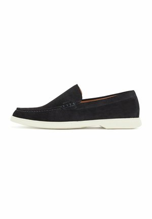 Sort ruskind slip-on loafer med hvid gummisål, rundet snude og mokkasinsting langs øverste kant.