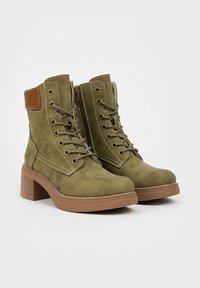 Bottines en daim vert avec un accent en cuir marron. Présente un devant à lacets, une fermeture éclair sur le côté et un talon épais marron.