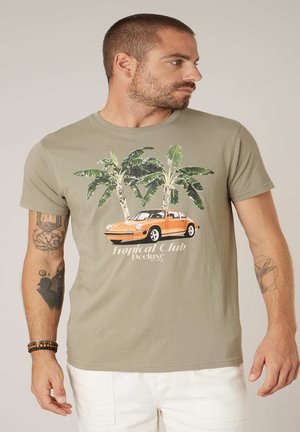 Homme aux cheveux courts et tatouages portant une chemise vert olive avec une voiture vintage orange et deux palmiers, accompagnée du texte "Tropical Club Deluxe".