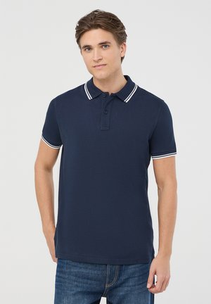 Granatowa koszulka polo z zapięciem na trzy guziki, białym prążkowanym kołnierzykiem i krótkimi rękawami. Posiada gładką, teksturowaną tkaninę.