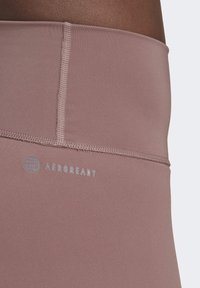 Leggings atletici AEROREADY rosa con una texture liscia, dotati di una vita cucita e dettagli logo stampati. Design regolabile e aderente.