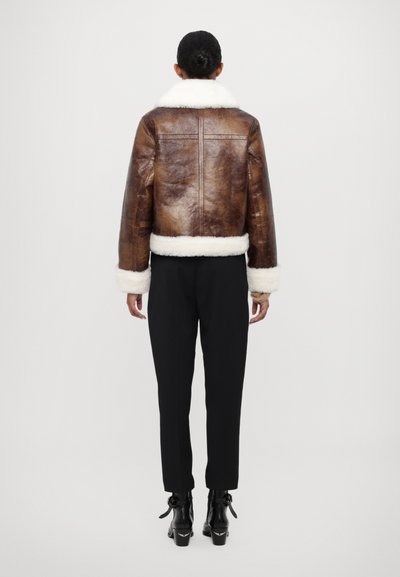 Brun læder cropped jakke med hvidt shearling krave og manchetter, der har en glat tekstur og struktureret design, parret med sorte bukser.