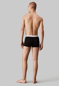 Boxers ajustados pretos com um cós elástico branco em destaque com o logo da Calvin Klein. O tecido é suave e ajustado, oferecendo uma silhueta justa.