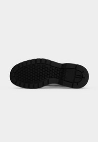 Semelle de chaussure noire avec motif de bande de roulement texturé comprenant des formes hexagonales et rectangulaires pour l’adhérence et la durabilité.