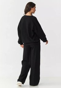 Czarny, oversize sweatshirt i szerokie spodnie, wykonane z miękkiego materiału. Posiada obniżone ramiona, luźny krój oraz ściągacze przy mankietach.