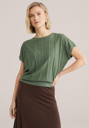 Top verde a maniche corte in maglia con trama a coste verticali, vestibilità comoda e scollo arrotondato, abbinato a una gonna marrone.