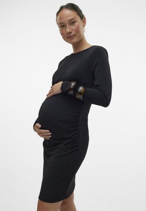Crna haljina dugih rukava od rastezljivog jerseya s detaljima nabrane tkanine sa strane, prilagođenog kroja i okruglog izreza. Dodaci uključuju dva smeđa narukvice.