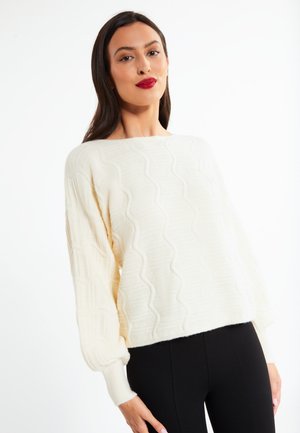 Cremefarvet, struktureret sweater med et bølgende mønster og ballonærmer, i cropped længde, parret med sorte leggings. Blødt materiale, afslappet pasform.