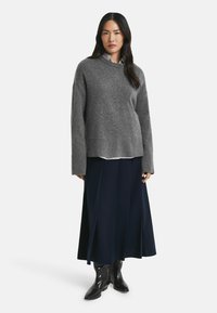 Grauer gestrickter Pullover mit langen Ärmeln und rundem Ausschnitt. Kombiniert mit einem marineblauen Faltenrock und schwarzen spitzen Stiefeln.