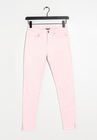Pantalones ajustados de color rosa claro con bolsillos delanteros y traseros, cierre de botón y pequeñas aberturaslaterales en los tobillos, colgados de un perchero negro.