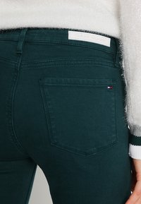 Jeans de color verde oscuro con un diseño de bolsillo trasero estándar, elaborados en denim con una textura mate. Incluye una etiqueta de marca en la cinturilla.