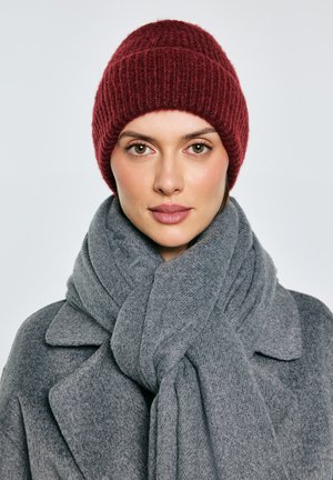 Bordowa dzianinowa czapka, szary oversize'owy wełniany szalik i szary płaszcz z detalicznym kołnierzem. Gładkie tekstury i ciepły kontrast kolorów.