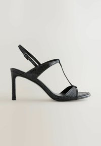 Sandale cu toc înalt din piele lacuită neagră, cu un model texturat de reptilă, vârf deschis, design cu curea în formă de T și cataramă ajustabilă la gleznă.