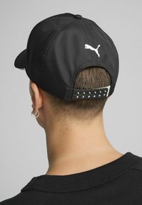 Musta müts, millel on kõver visor, valmistatud siledast kangast, ja tagaküljel on valge logo ning tekstuuriga rihm, millel on peegeldavad aktsendid.