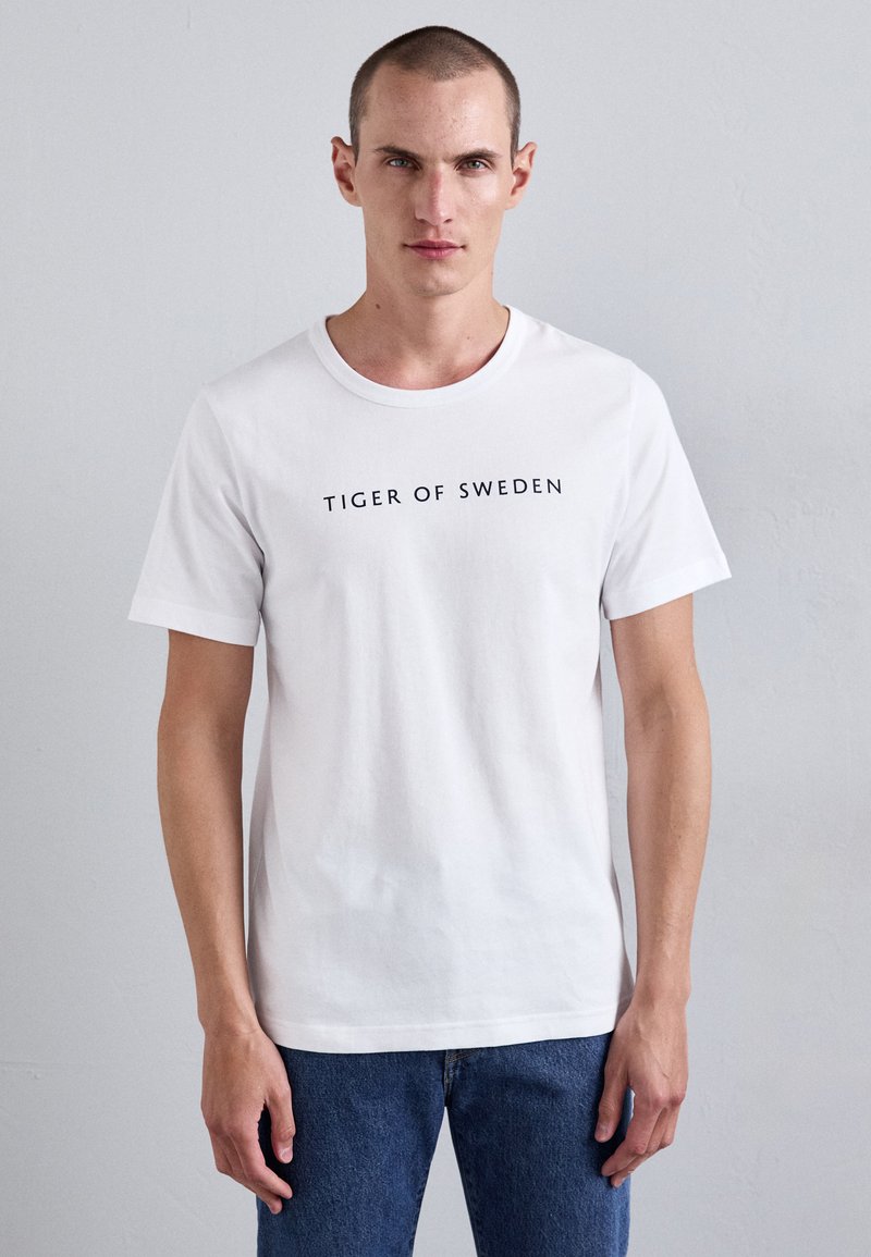Hvit bomulls T-skjorte med teksten "TIGER OF SWEDEN" i svart på fronten, med korte ermer og rund halsdesign.