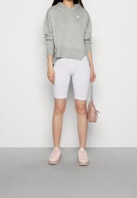 Grå hoodie med framficka och huva, vita shorts, rosa sneakers och en liten rosa handväska med kedjesnodd.