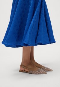 Peščane slingback balerinke s koničastim nosom, okrašene s kamni, v kombinaciji z modrim midi krilom z teksturo, ki vsebuje cvetlične vzorce.