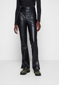 Svarta imitationläderbyxor med utsvängd benform, framseamsdetaljer och slitsar vid anklarna, i kombination med blommönstrade skor. Slät, glansig yta.