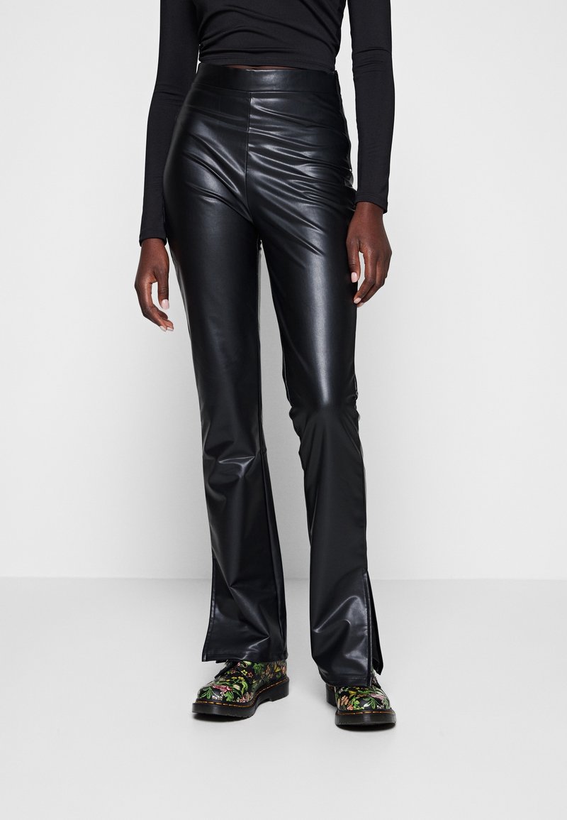 Svarta imitationläderbyxor med utsvängd benform, framseamsdetaljer och slitsar vid anklarna, i kombination med blommönstrade skor. Slät, glansig yta.