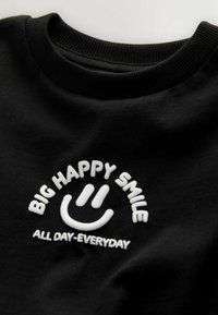 Black cotton sweatshirt featuring white embroidered text: "BIG HAPPY SMILE" above a smiley face and "ALL DAY-EVERYDAY" below. Ribbed collar.