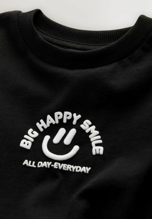 Schwarzer Baumwoll-Sweatshirt mit weißer Stickerei: "BIG HAPPY SMILE" über einem Smiley-Gesicht und "ALL DAY-EVERYDAY" darunter. Gerippter Kragen.