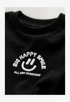 Fekete pamut pulóver fehér hímzett felirattal: "BIG HAPPY SMILE" egy mosolygós arc felett, és "ALL DAY-EVERYDAY" alatta. Bordázott gallér.