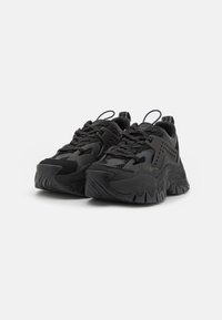 Scarpe da ginnastica nere con suola in gomma testurizzata, tomaia in rete e dettagli moldati. Presentano una chiusura con lacci e un tassello alla parte posteriore.