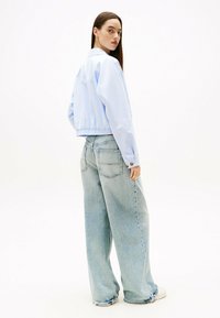 Giacca cropped azzurro chiaro con una texture liscia, abbinata a pantaloni in denim chiaro a gamba larga dotati di tasche posteriori e orli sfrangiati.