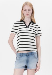 Randig kortärmad polo med vit och svart, med en v-ringning och strukturerad tyg. Kombinerad med ljusblå denimshorts.