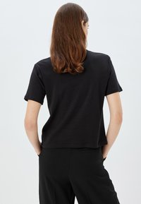 Sort kortærmet T-shirt med afslappet pasform, blødt bomuldsstof og rund halsudskæring. Enkel design med lige kant.