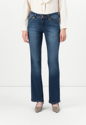 Jeans en denim bleu foncé avec une coupe évasée, dotés d'une taille haute, de poches avant et de détails de couture subtils. Associés à des talons beiges.