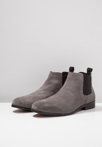Bottes chevilles en daim gris avec une texture lisse, des panneaux latéraux élastiques et un talon bas. Dotées d'une languette à l'arrière pour un enfilage facile.