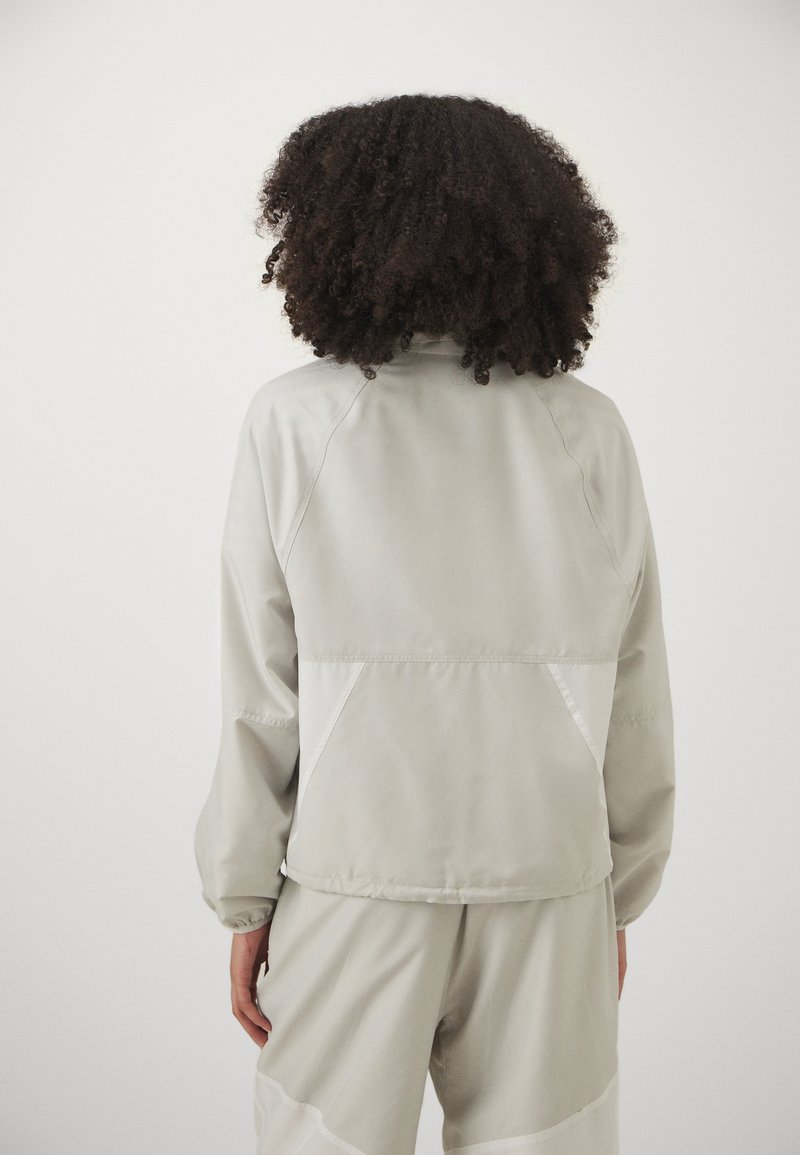 Lichtgrijze lichtgewicht jas met een hoge kraag, raglanmouwen en contrasterende witte zijpanelen. Gladde textuur, geschikt voor casual draag.