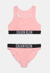 Ροζ μαγιό δύο τεμαχίων Calvin Klein με μαύρες ελαστικές ζώνες που φέρουν το άσπρο λογότυπο Calvin Klein, τοπ σε μορφή αθλητικού σουτιέν και σλιπ μπικίνι.