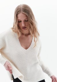 Maglione a V blu con una texture a costine, spalle scese e spacchi laterali, realizzato in materiale morbido e leggero.