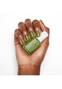 Groene nagellakfles naast een hand met groene gemanicuurde nagels. De fles heeft een witte dop en reliëfmerk op de zijkant.