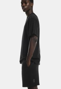 Tricou din bumbac negru cu o croială lejeră, având mâneci scurte. Asortat cu pantaloni scurți din bumbac negri și un detaliu subtil al logo-ului aproape de tiv.